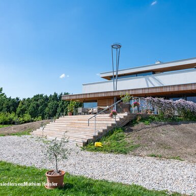 Der moderne Hof mit einer großen Terrasse und Sitzgelegenheiten, über eine breite Holztreppe zugänglich, umgeben von einer gepflegten Grünfläche.