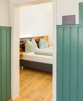 Doppelzimmer im Bed and Breakfast mit Bett, Holz-Kopfteil und grüner Bettwäsche auf Holzfußboden.