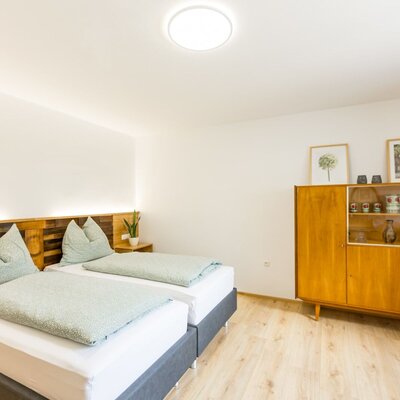 Schlafzimmer im Bed and Breakfast mit zwei Einzelbetten, einem Holzkopfteil mit integrierter Beleuchtung und einem Sideboard.