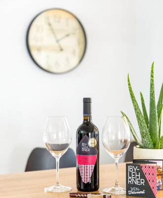 Eine Flasche IBY-LEHNER Rotwein und zwei Weingläser auf dem Holztisch des Bed and Breakfast.