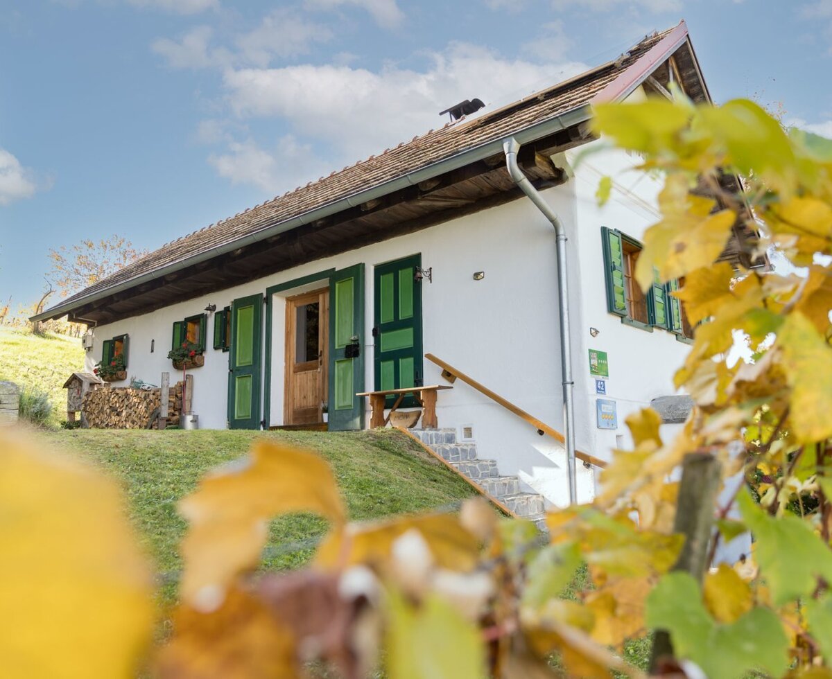 Das einladende Kellerstöckl mit seinen charakteristischen grünen Fensterläden, umgeben von einem grünen Hang und herbstlicher Natur.