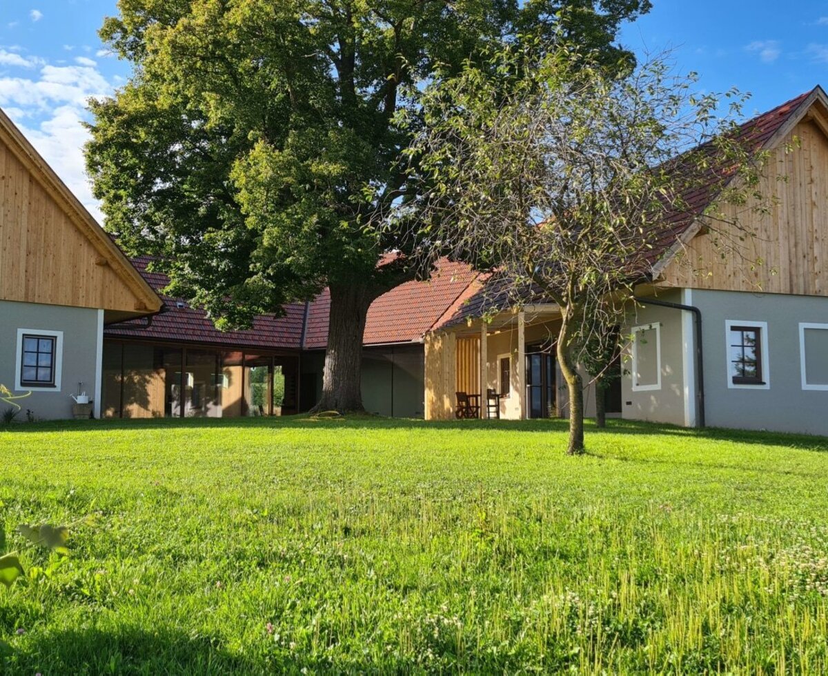 Außenansicht des revitalisierten Dreikanthofs mit großer Grünfläche, alten Bäumen und Ansicht der umliegenden Weingärten.