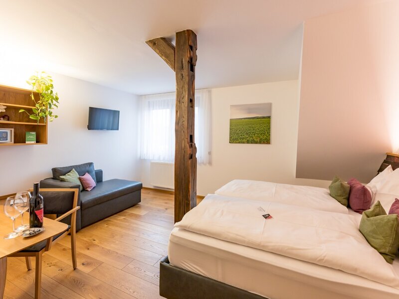 Doppelzimmer im Hof mit Doppelbett, Sofa, Essbereich, Fernseher, Safe und Holzbalken.