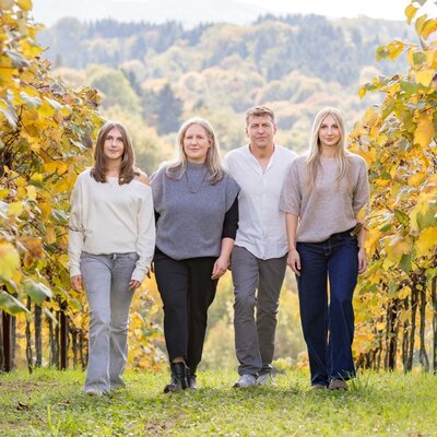 Die Gastgeberfamilie geht durch die herbstlichen Weingärten des Hauses, umgeben von hügeliger Landschaft.