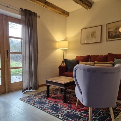 Der Wohnbereich im Hof bietet ein rotes Sofa, einen lavendelfarbenen Sessel, einen Holztisch, Holzbalken an der Decke und Zugang zum Garten.