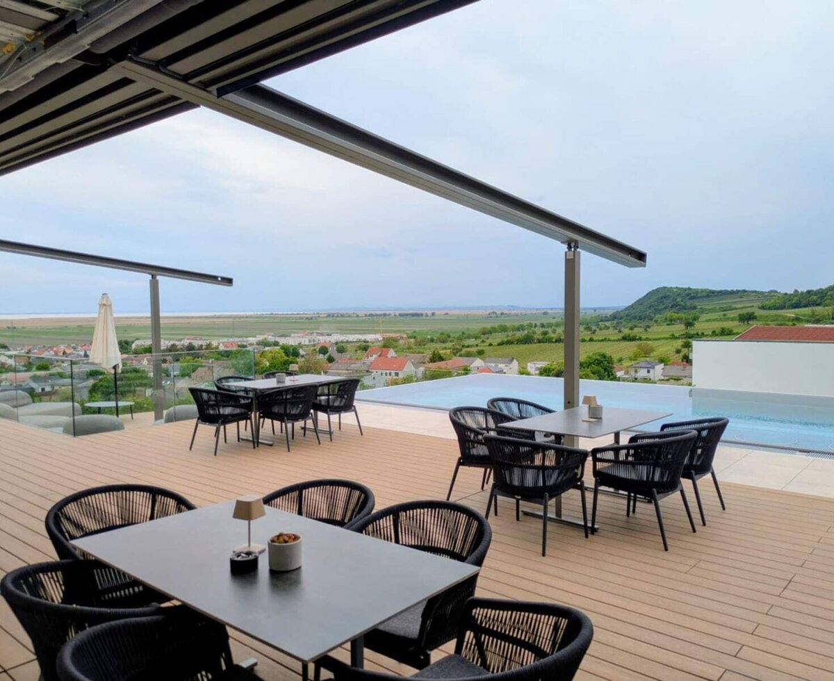 Die Terrasse des Bauernhofs mit Tischen, Stühlen und einem Infinity-Pool bietet einen Ausblick auf die Landschaft und den See.