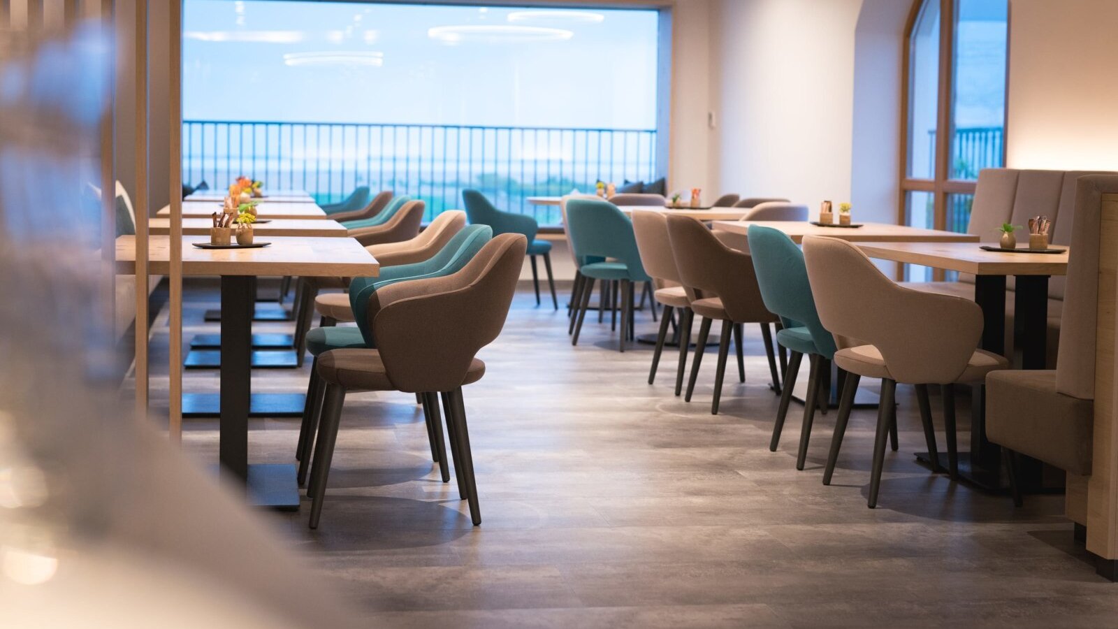 Der Aufenthaltsraum im Hof mit Tischen, Stühlen und großen Fenstern.