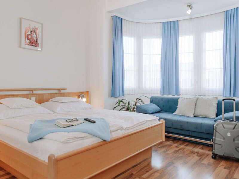 Schlafzimmer im Haus mit Doppelbett, einem Sofa und Fenstern mit blauen Vorhängen.