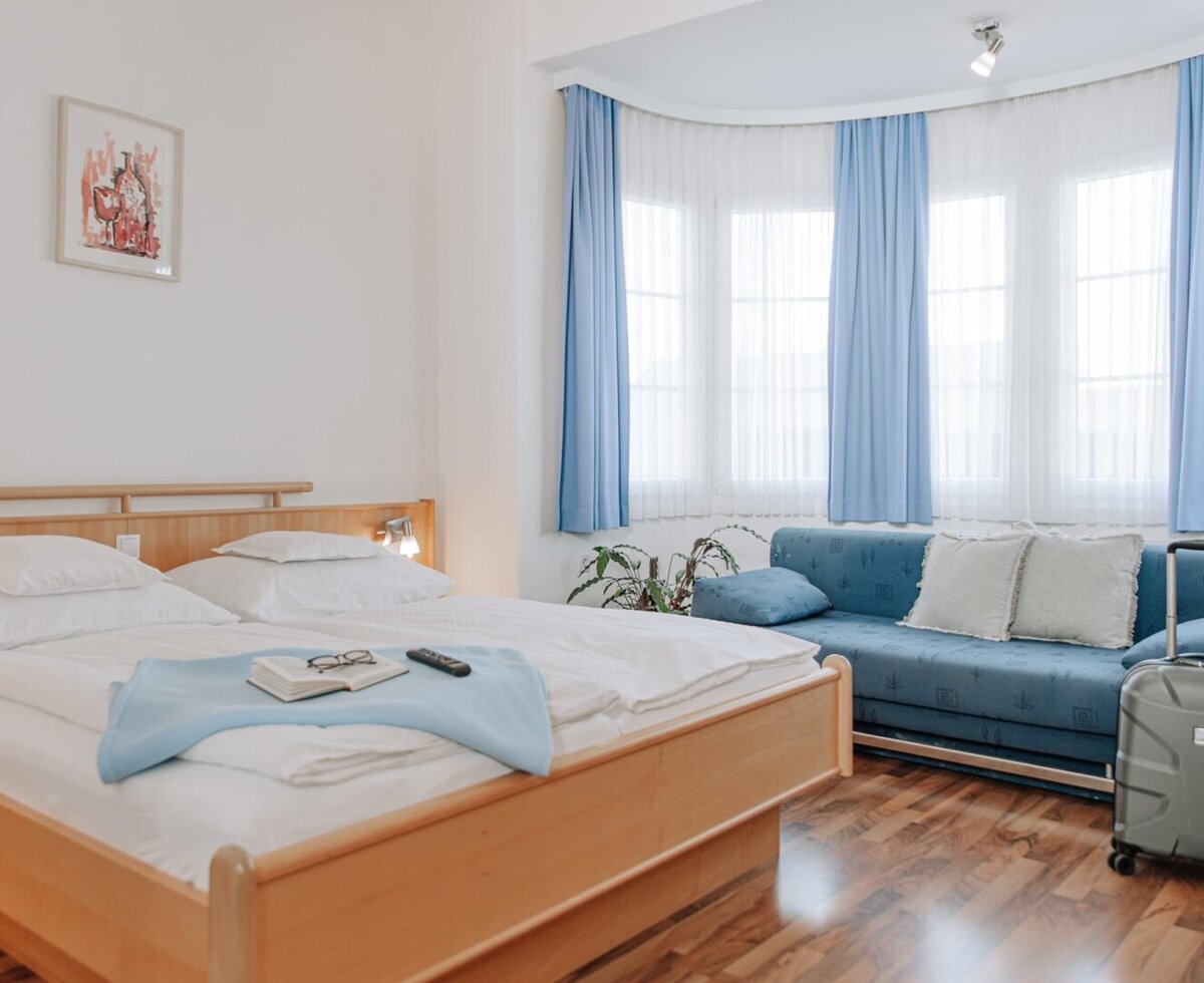 Schlafzimmer im Haus mit Doppelbett, einem Sofa und Fenstern mit blauen Vorhängen.