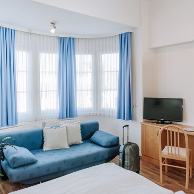 Zimmer im Haus mit Bett, blauem Sofa, Erkerfenster, Kabel-TV, Schreibtisch und Kleiderschrank.