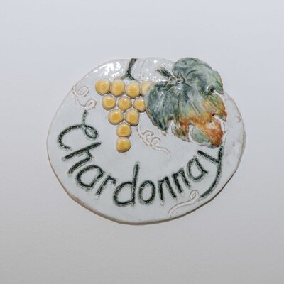 Ein rundes Keramikschild mit der Aufschrift 'Chardonnay' und einem Relief von Weintrauben und einem Blatt im Haus.