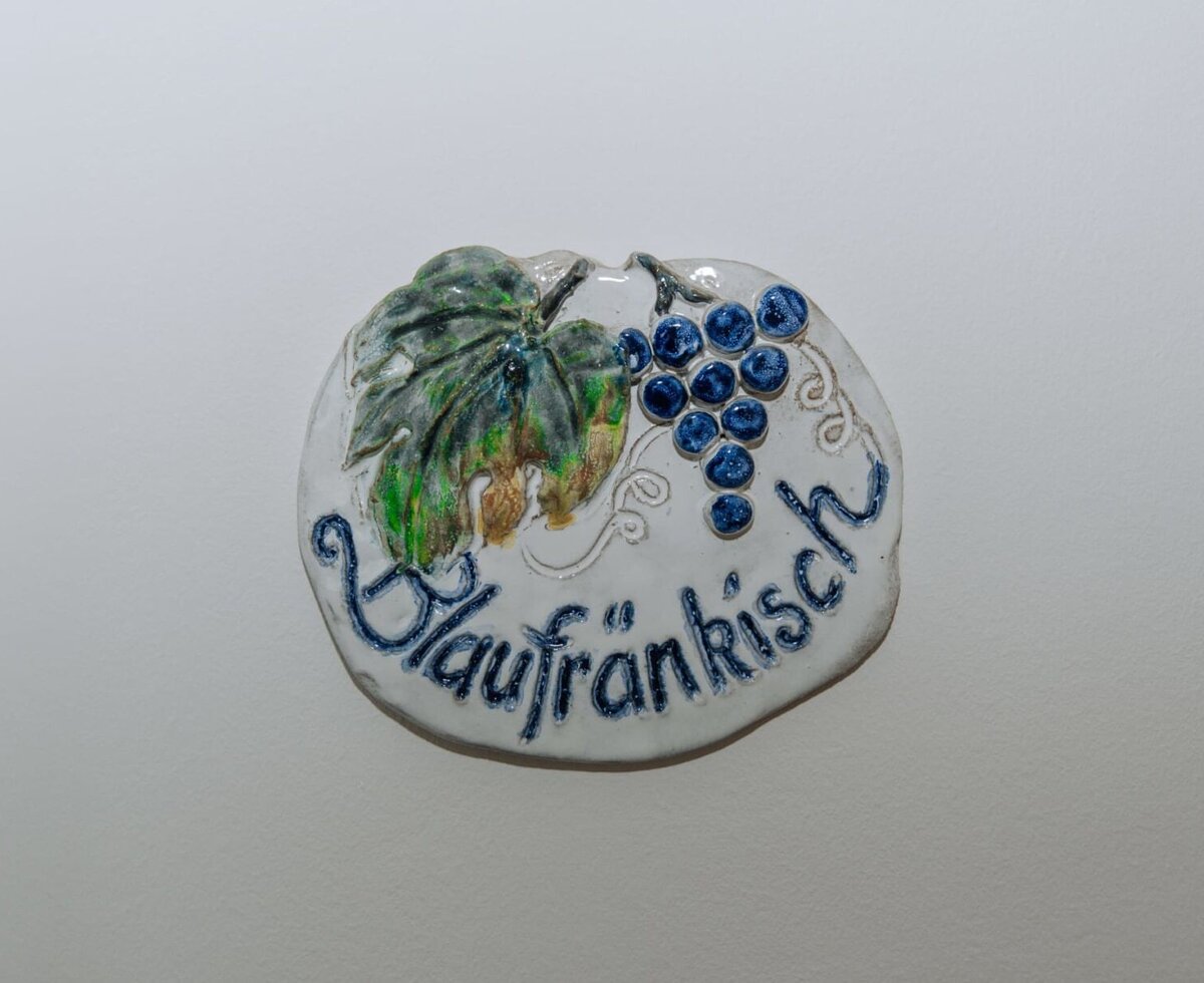 Keramikplakette im Haus mit 'Blaufränkisch' Schriftzug, Trauben und Weinblattmotiv.