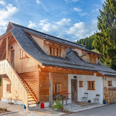 Das Ferienhaus mit Holzfassade, weiß verputzten Wänden, einer Außentreppe und einer Terrasse mit Sitzgelegenheiten.