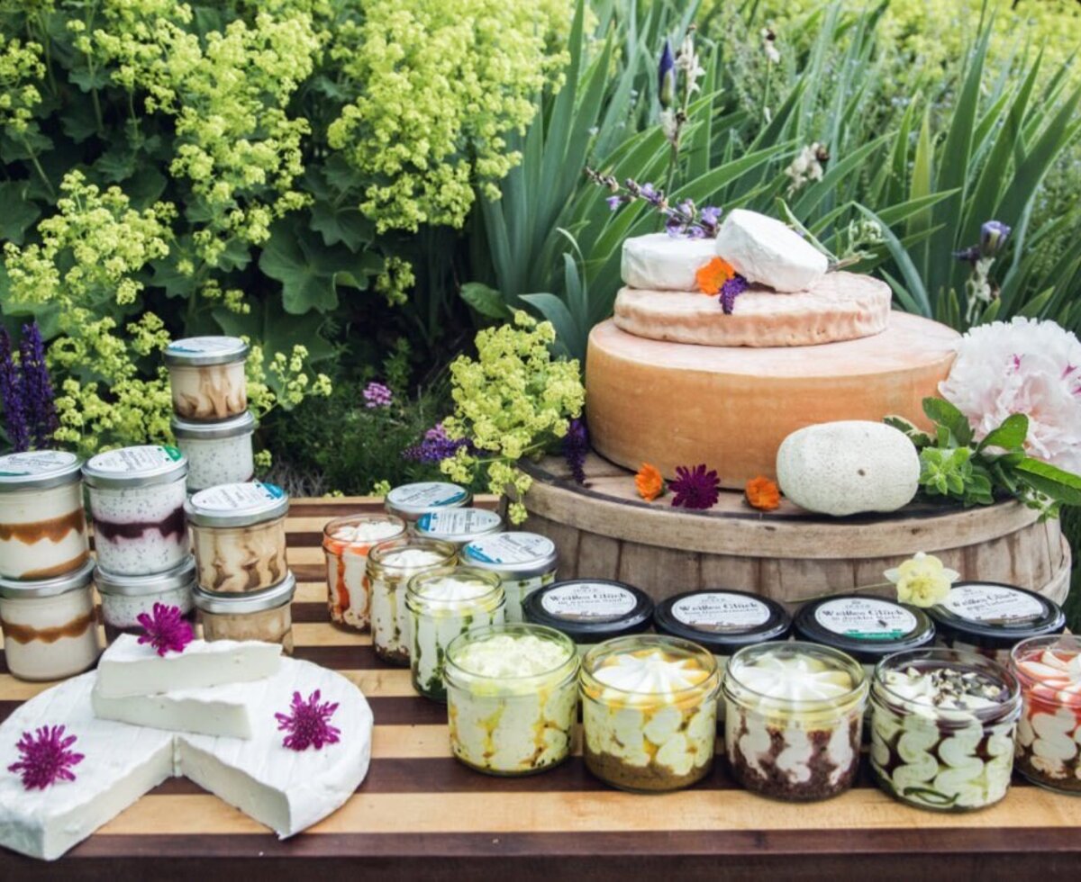 Eine Auswahl an Käsesorten und Milchprodukten, darunter große Käselaibe, Frischkäse und mehr in Gläsern, die im Ferienhaus angeboten werden.