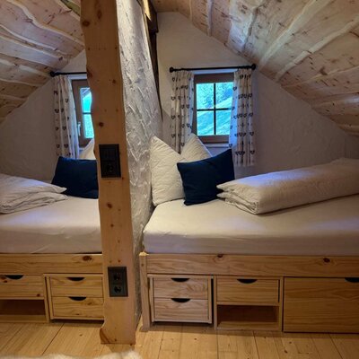Ein gemütlicher Schlafraum der Alm mit urigen Holzbetten unter einer Dachschräge und integrierten Schubladen.