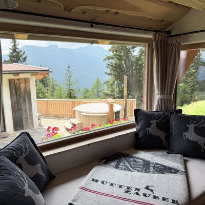 Im Zirbenzimmer lädt ein behaglicher Fensterplatz zum Verweilen ein – mit Blick auf die Bergwelt, den privaten holzbeheizten Hot Tub und das separate Saunahaus auf der Terrasse.