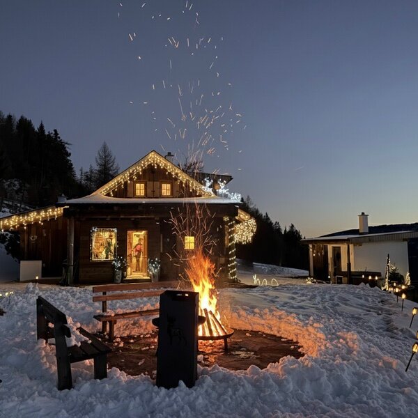 Ein Winterabend an der Hütte: knisterndes Feuer, sanftes Lichterglanz und die verschneite Bergkulisse schaffen eine besondere Atmosphäre.