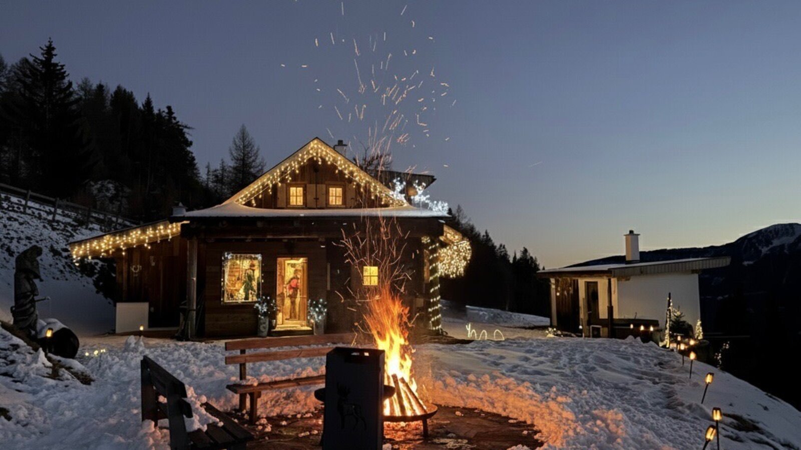 Ein Winterabend an der Hütte: knisterndes Feuer, sanftes Lichterglanz und die verschneite Bergkulisse schaffen eine besondere Atmosphäre.