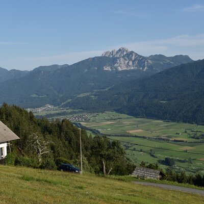 Blick von der Alm auf das Tal mit Feldern, einem Dorf und den umliegenden Bergen.