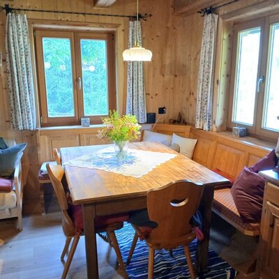 Essbereich mit Holztisch, Eckbank und Stühlen, umgeben von Holzwänden und Fenstern.