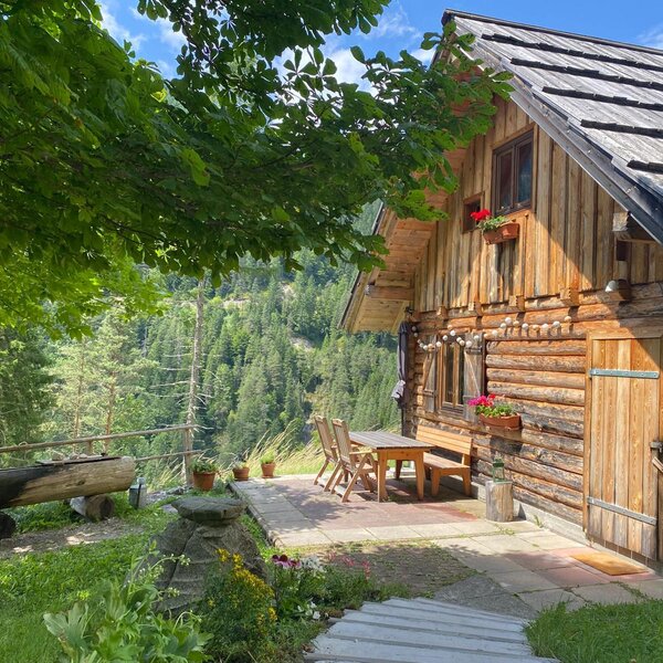Die Außenseite des Bed and Breakfast mit einer Holzfassade, einem gepflasterten Sitzbereich im Freien und Blick auf die bewaldete Berglandschaft.