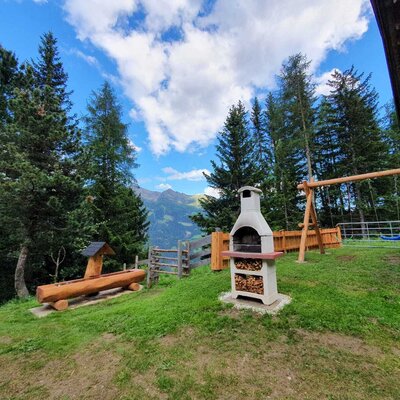 Der Außenbereich der Alm bietet einen Grillplatz, eine Schaukel und einen Holzbrunnen mit Bergblick.