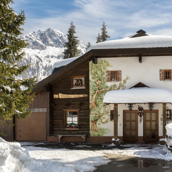 Die schneebedeckte Alm mit traditioneller Fassade und Blick auf die umliegenden Berge.
