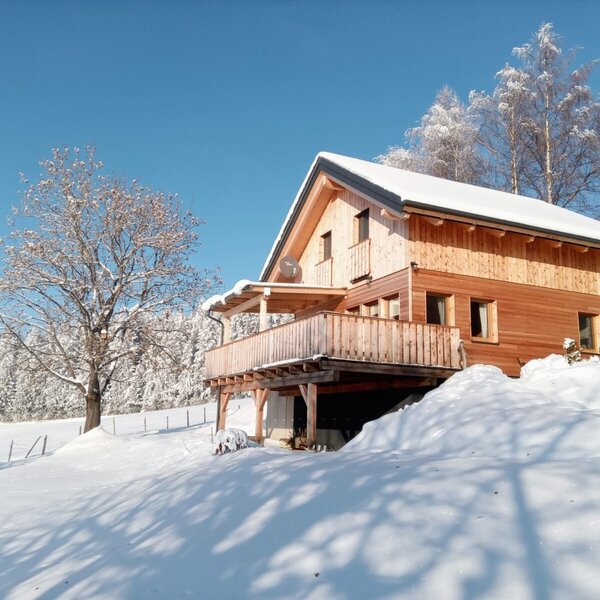 Das Auszeit-Almhaus im Winter, mit Holzfassade, verschneiter Umgebung und großer Sonnenterrasse.