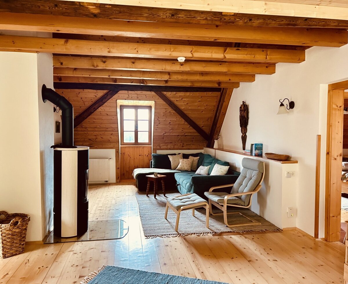 Der Wohnbereich des Ferienhauses mit Kaminofen, Sofa, Sessel und Holzbalkendecke.