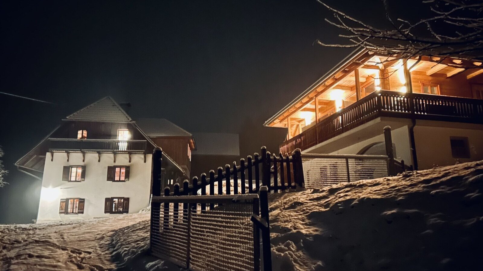 Außenansicht des Ferienhauses bei Nacht, mit Schnee und hell erleuchteten Fenstern und Balkonen.