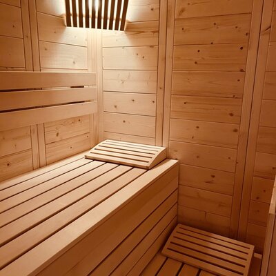 Die Holzsauna im Ferienhaus mit Sitzbänken und indirekter Beleuchtung.