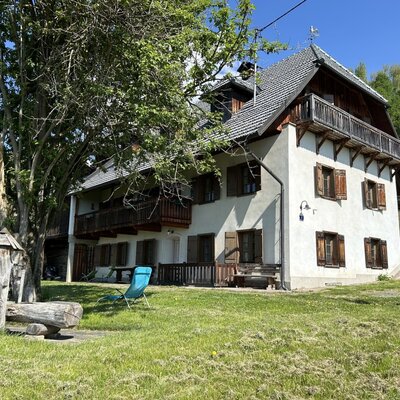 Das Ferienhaus von außen mit weißer Fassade, Holzfensterläden, Balkonen, einer Rasenfläche und einem Holzbrunnen.