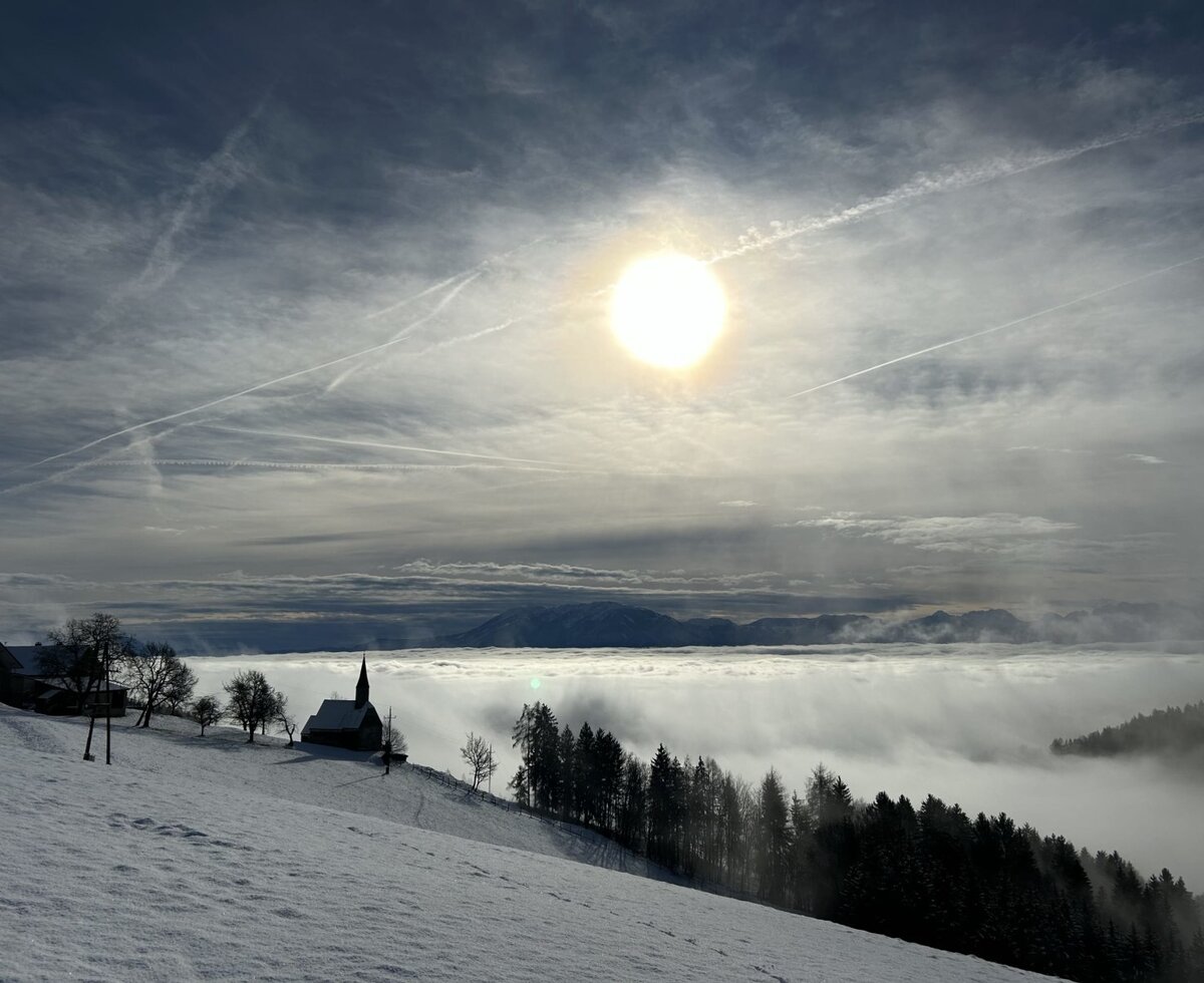 Die verschneite Berglandschaft mit einer Kirche, Nebelmeer und Sonnenschein in der Umgebung des Ferienhauses.