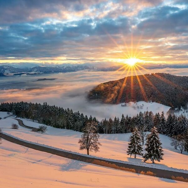 Die winterliche Landschaft rund um den Bauernhof bei Sonnenaufgang, mit verschneiten Wäldern, Hügeln und einem nebelverhangenen Tal.