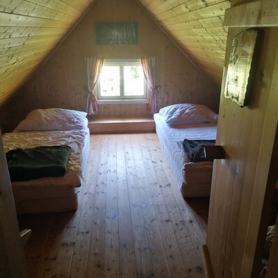 Dachzimmer der Alm mit zwei Einzelbetten, Holzvertäfelung und einem Fenster.