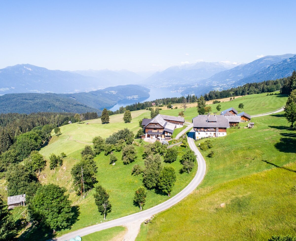 Der Bauernhof in ländlicher Umgebung, umgeben von grünen Wiesen und Wäldern, bietet einen Blick auf einen See und die Berge.