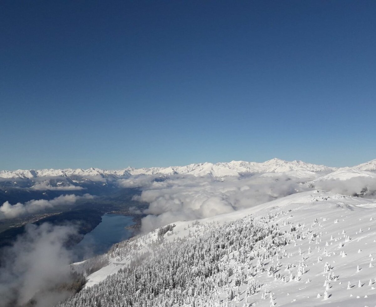 Winterliche Berglandschaft mit See und schneebedeckten Wäldern in der Umgebung des Bauernhofs.