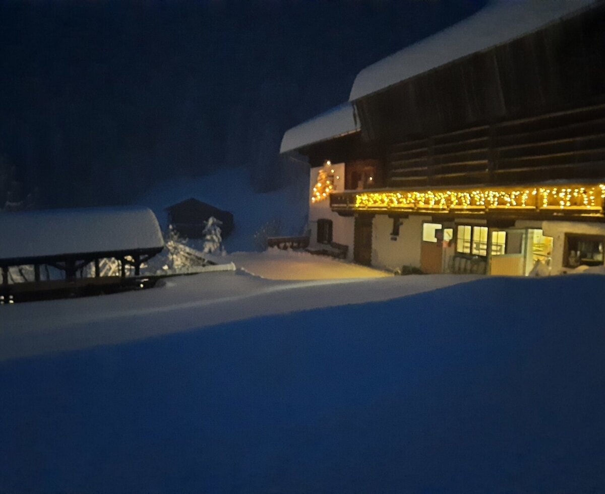 Der verschneite Bauernhof am Abend mit stimmungsvoll beleuchteten Balkonen und einer dicken Schneedecke.