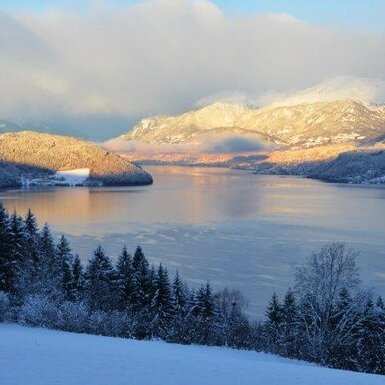Blick vom Bauernhof auf den winterlichen Millstätter See und die schneebedeckten Berge.