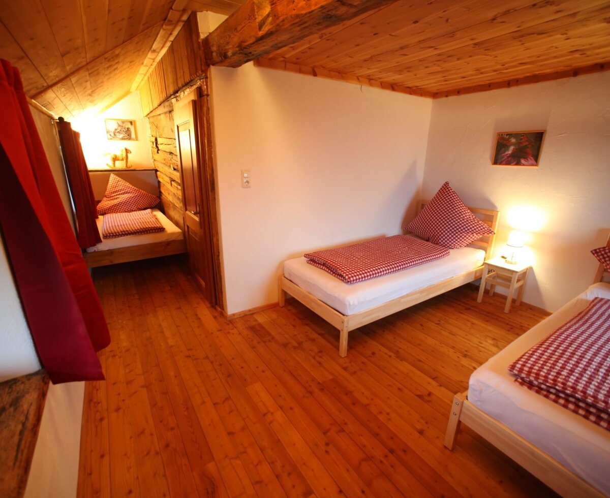 Schlafzimmer im Bauernhof mit drei Einzelbetten, Holzboden, rot-weiß karierter Bettwäsche und einem Bett in einer Nische.
