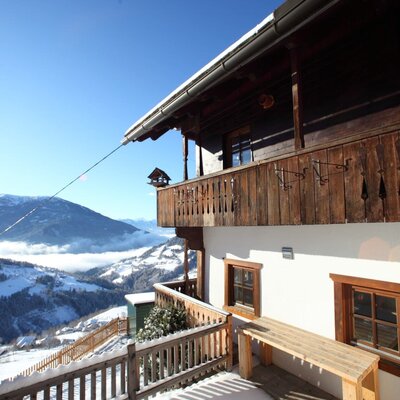 Außenansicht des Bauernhofs mit Holzbalkon, einer schneebedeckten Terrasse und weitem Blick auf die verschneiten Berge.
