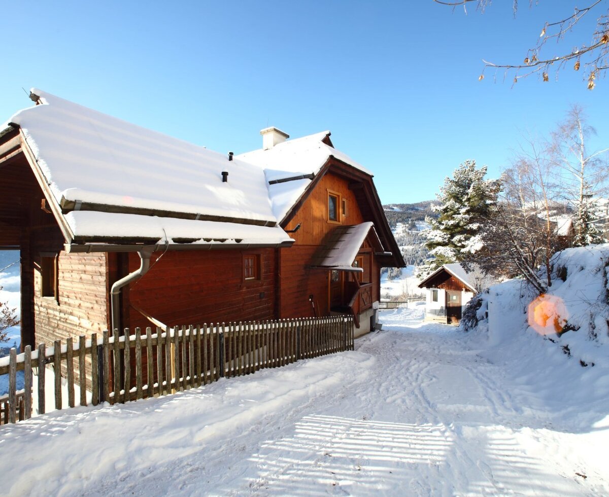 Der Bauernhof mit seinem Holzgebäude, bedeckt mit Schnee, und einem verschneiten Weg, der zum Eingang führt.