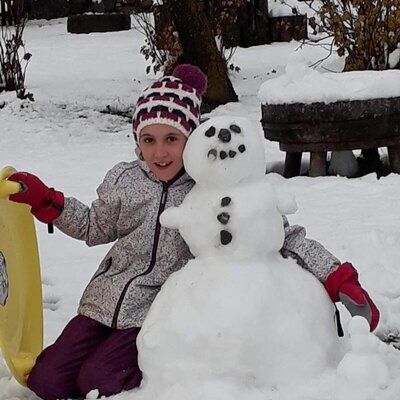 Ein Kind mit einem Schneemann im verschneiten Außenbereich des Bauernhofs.