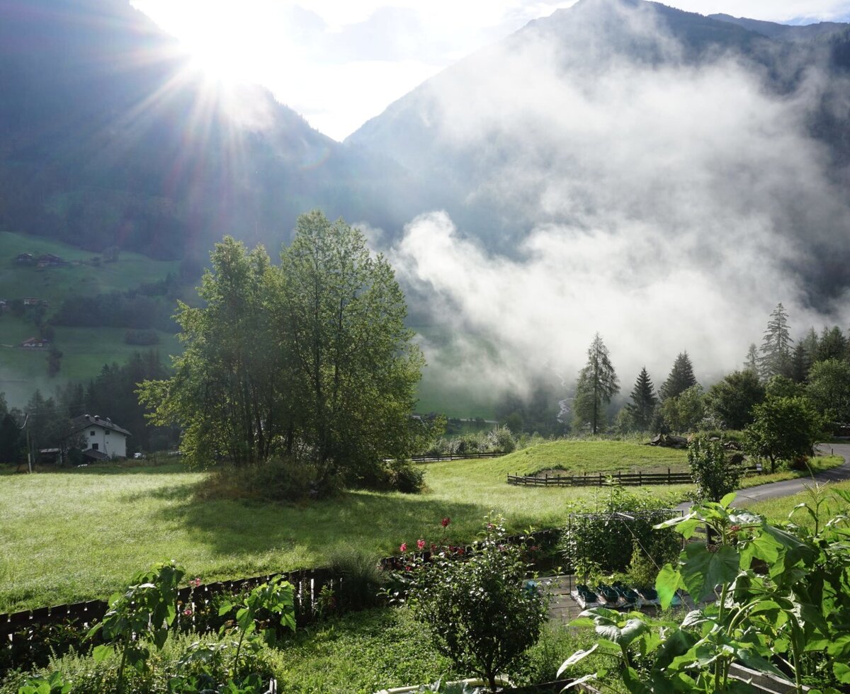 Blick auf die Berge des Mölltals mit morgendlichem Nebel und sonnenbeschienenen Feldern vom Bauernhof aus.