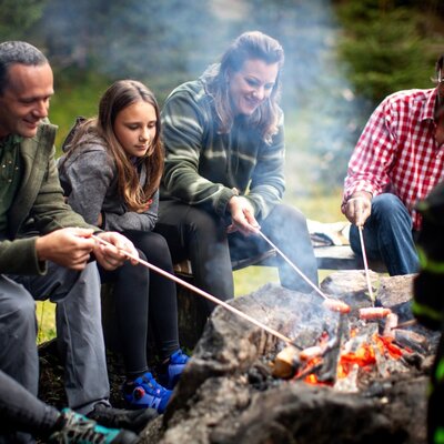 Gäste braten Würstchen am Lagerfeuer auf der Alm.