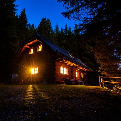 Die beleuchtete Alm bei Nacht, umgeben von Bäumen.
