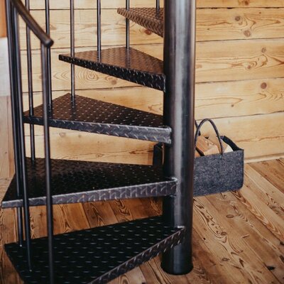 Schwarze Metall-Wendeltreppe mit Riffelblechstufen im Ferienhaus, ergänzt durch einen Korb mit Brennholz.