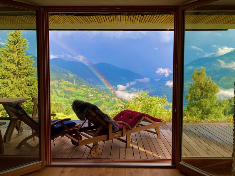Terrasse des Chalets mit Liegestühlen und Panoramablick auf das Tal und einen Regenbogen.