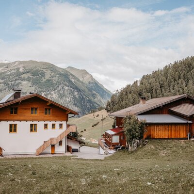 Der Bauernhof mit seinen Gebäuden inmitten der Berglandschaft und umgeben von Wald.