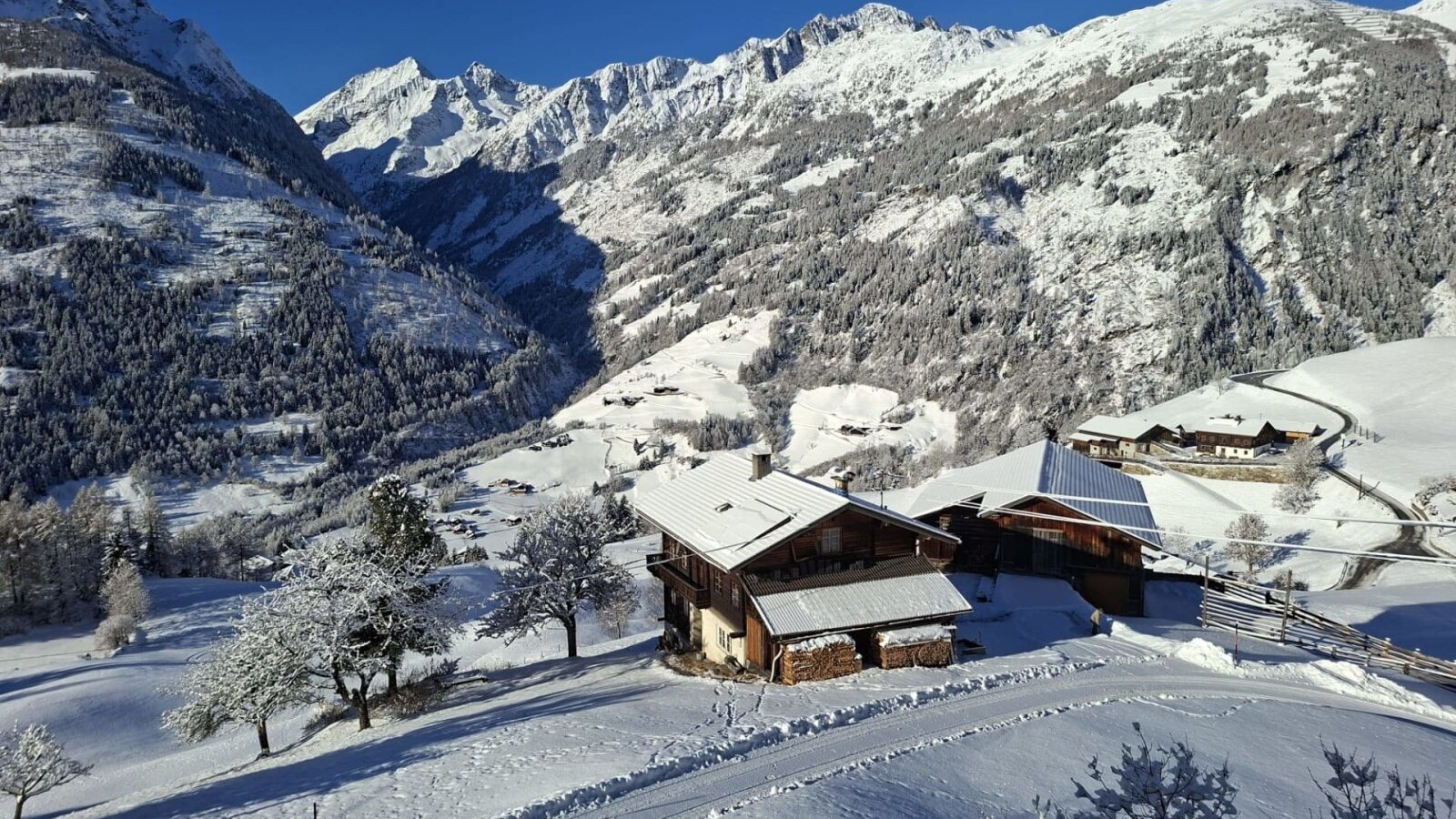 Der Bauernhof in einer verschneiten Berglandschaft mit Blick auf die umliegenden Berge.